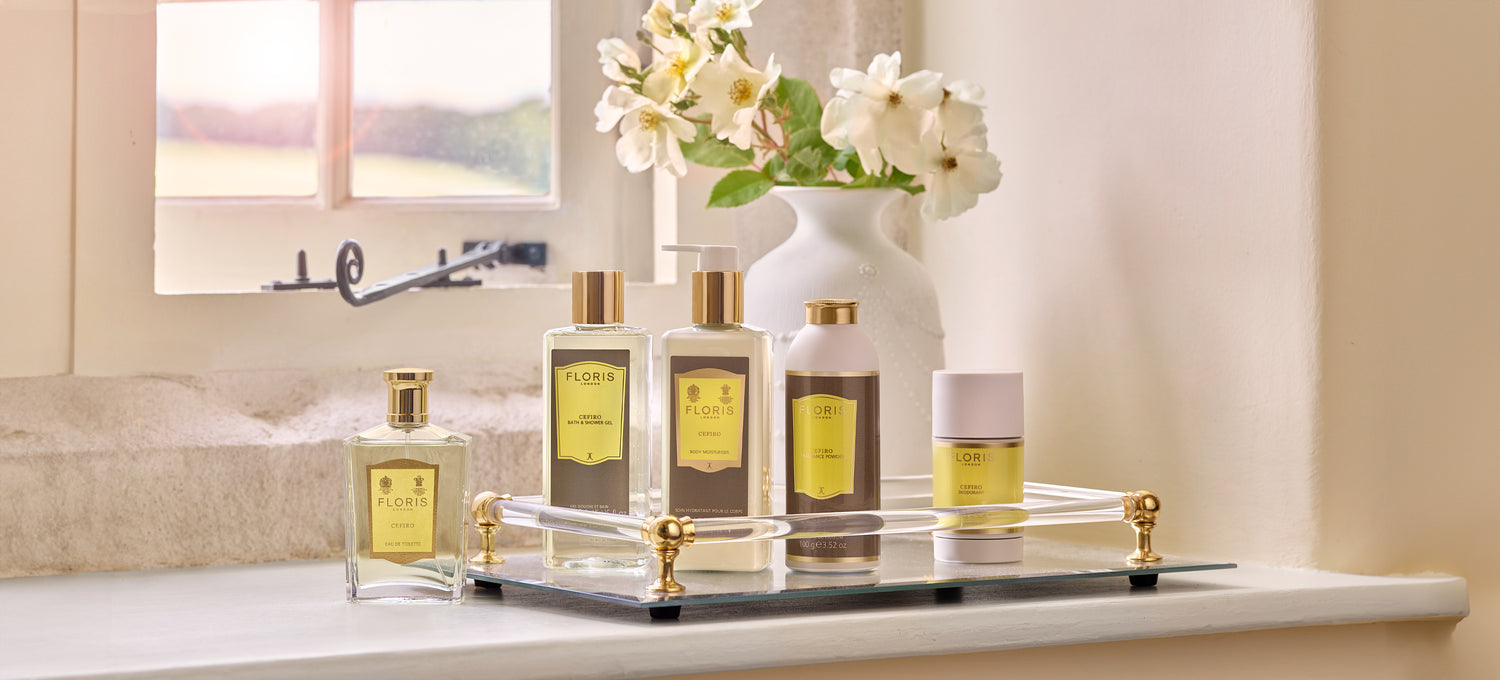 The Cefiro collection arranged on a mirrored tray, resting on a window ledge beside a vase of white flowers.