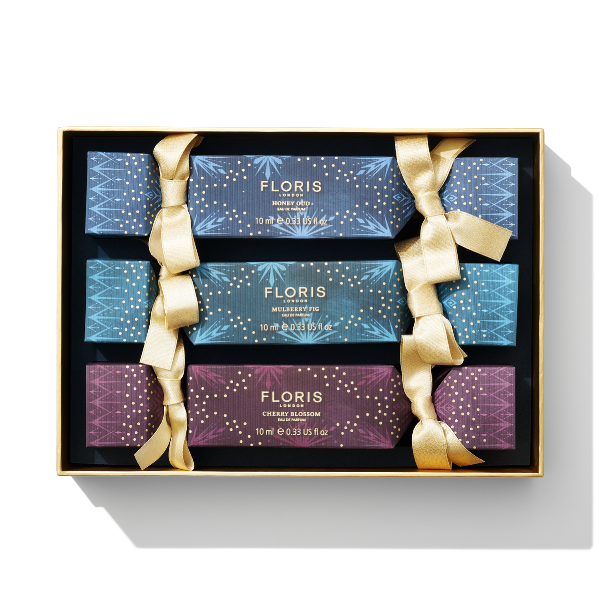 Introducing the Holiday Cracker Collection by Floris London EU: a set of four beautifully packaged fragrance bottles, each adorned with gold ribbons. Perfect for celebrations, this gift box includes enchanting scents of Honey Oud, Mulberry Fig, and Cherry Blossom.