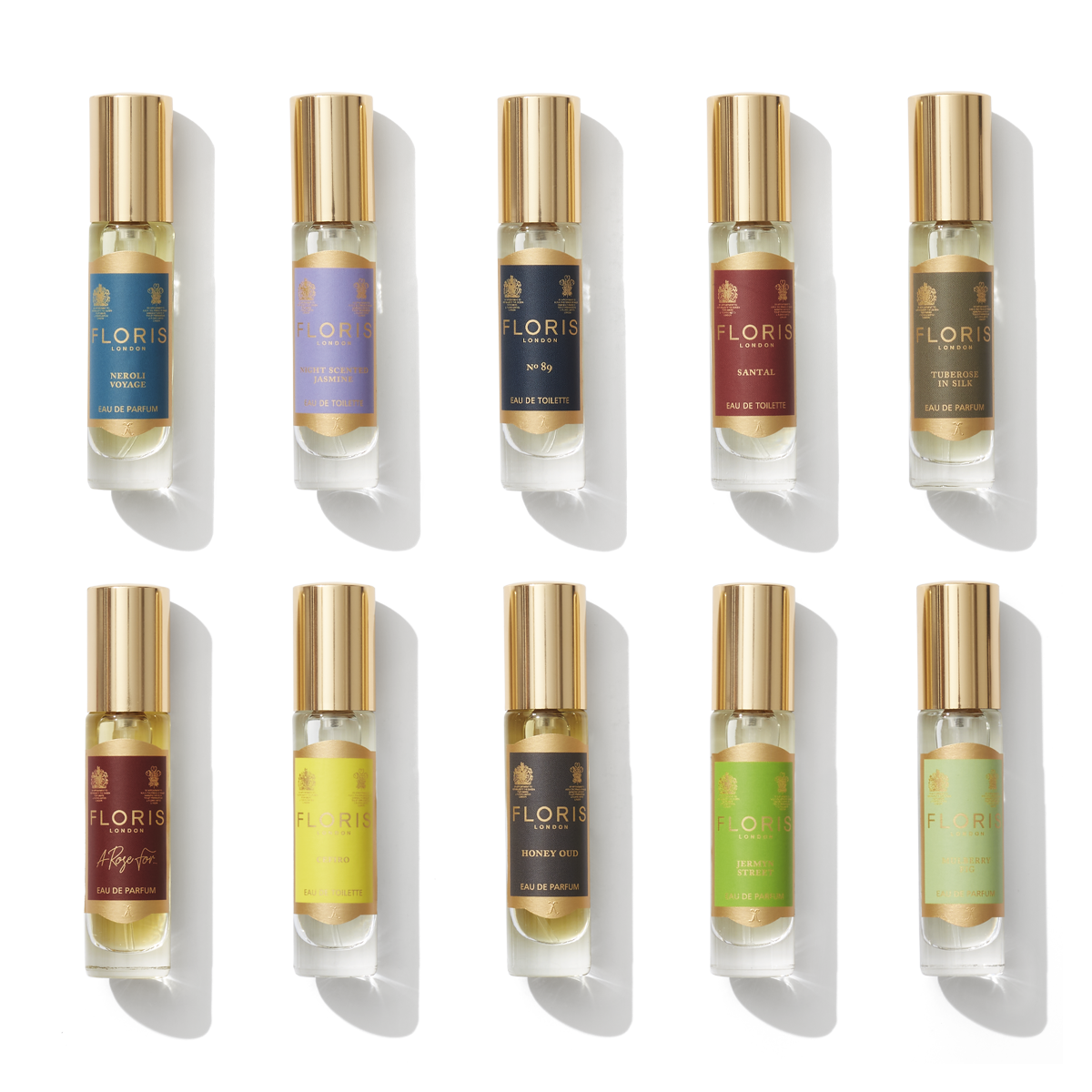 An ideal gift for the connoisseur, The Perfumer's Collection by Floris London EU features ten exquisite perfume bottles in a range of vibrant colors, each adorned with a gold cap, elegantly showcased in two rows against a pristine white backdrop.
