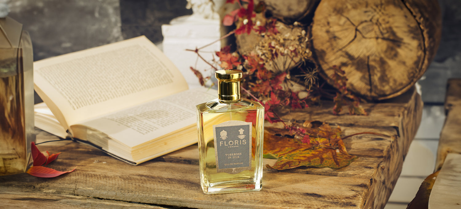 A Bottle of 'Tuberose in Silk', upon a wooden table with a open book and autumn foliage.