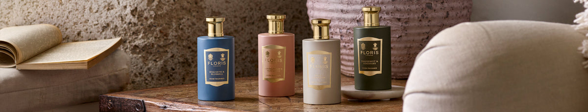 Four elegant perfume bottles on a rustic wooden table with an open book and a plush cushion nearby.