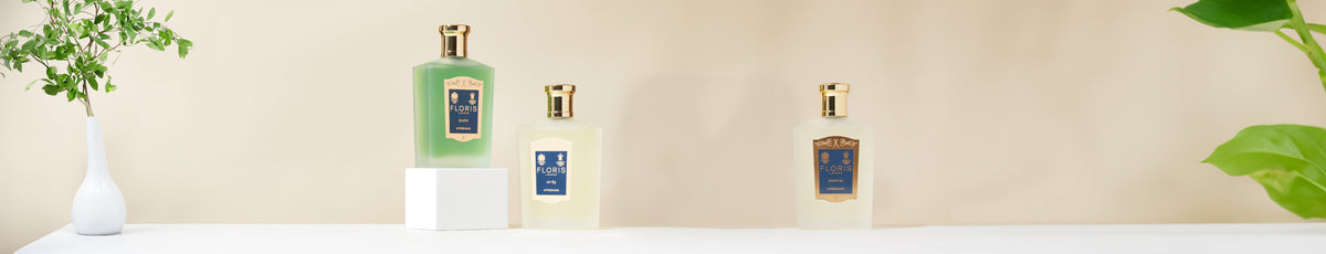 Three elegant bottles of bath products on a white surface, flanked by green plants on both sides.