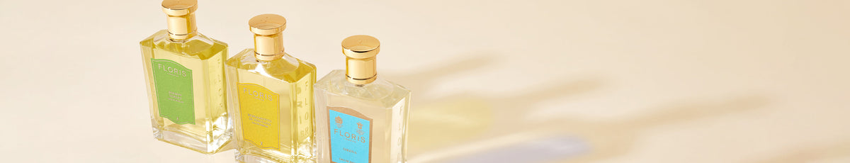Three Floris perfume bottles with gold caps are placed on a white shelf beside a framed painting.