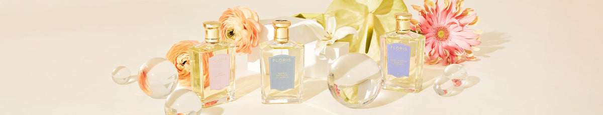 Four glass perfume bottles with gold caps are displayed on a wooden surface next to a shell decoration.