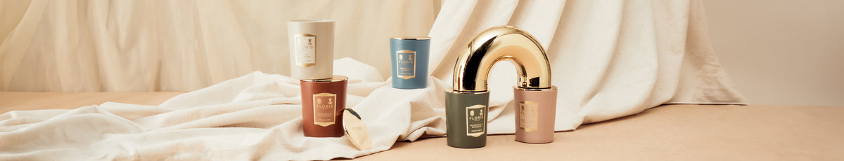 Aesthetic arrangement of colored candle jars and a gold arch on a draped fabric background.