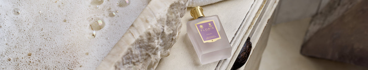 A perfume bottle lies on a beige surface next to a bubbling bath.
