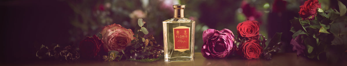 Perfume bottle labeled "Floris" surrounded by assorted roses and greenery on a blurred floral background.
