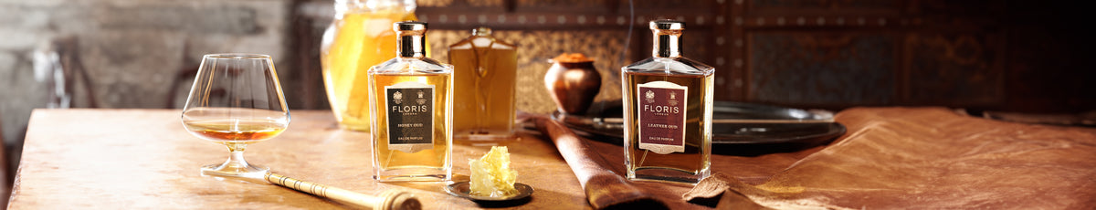 Assortment of whiskey bottles, glass of whiskey, honey, and brown papers arranged on a wooden table.