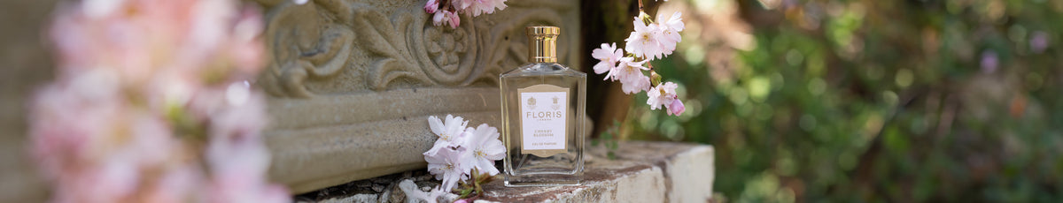 Perfume bottle on stone ledge with pink blossoms surrounding it, set against a blurred natural background.