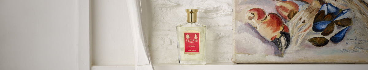 Perfume bottle labeled "Floris" next to a painting of birds on a shelf.