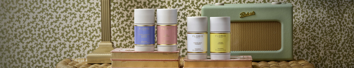Four perfume bottles on stacked books with a vintage radio and patterned wallpaper in the background.
