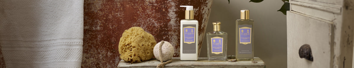 A set of luxury bath products with purple labels placed on a wooden surface alongside a sponge and a pumice stone.
