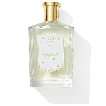 A clear glass bottle of Stephanotis - Eau de Parfum | Limited Edition by Floris London EU, featuring a gold cap and white label, cast a shadow on a pristine white background.