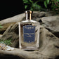 A glass bottle of Floris London 71/72 - Eau de Parfum, a Jermyn Street scent for men, sits on driftwood amid small plants and stones.