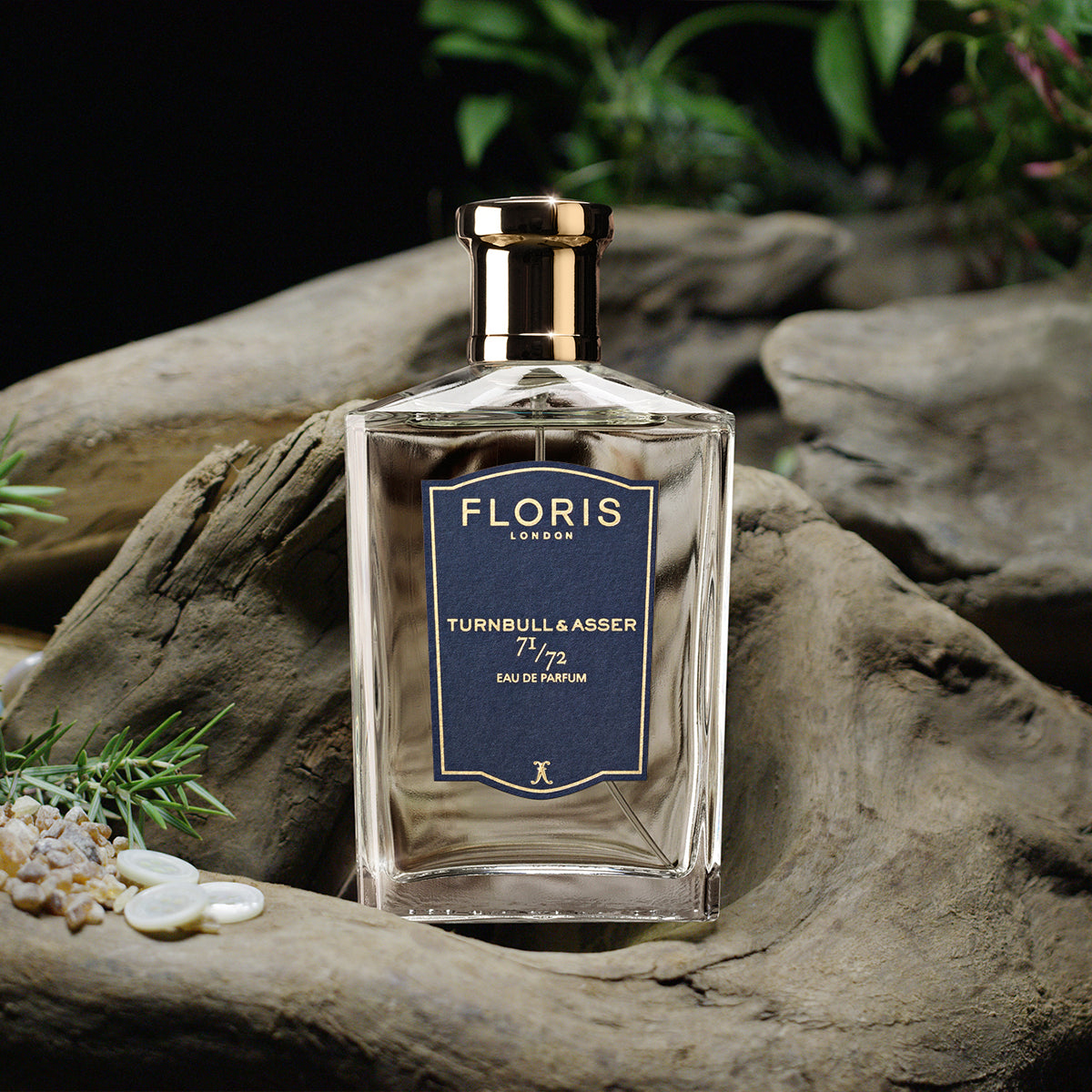 A glass bottle of Floris London 71/72 - Eau de Parfum, a Jermyn Street scent for men, sits on driftwood amid small plants and stones.