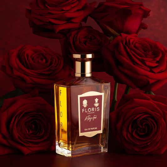 A bottle of Floris London’s A Rose For... Eau de Parfum stands upright amid red roses, embodying the allure of this oriental rose scent on a dark red background.