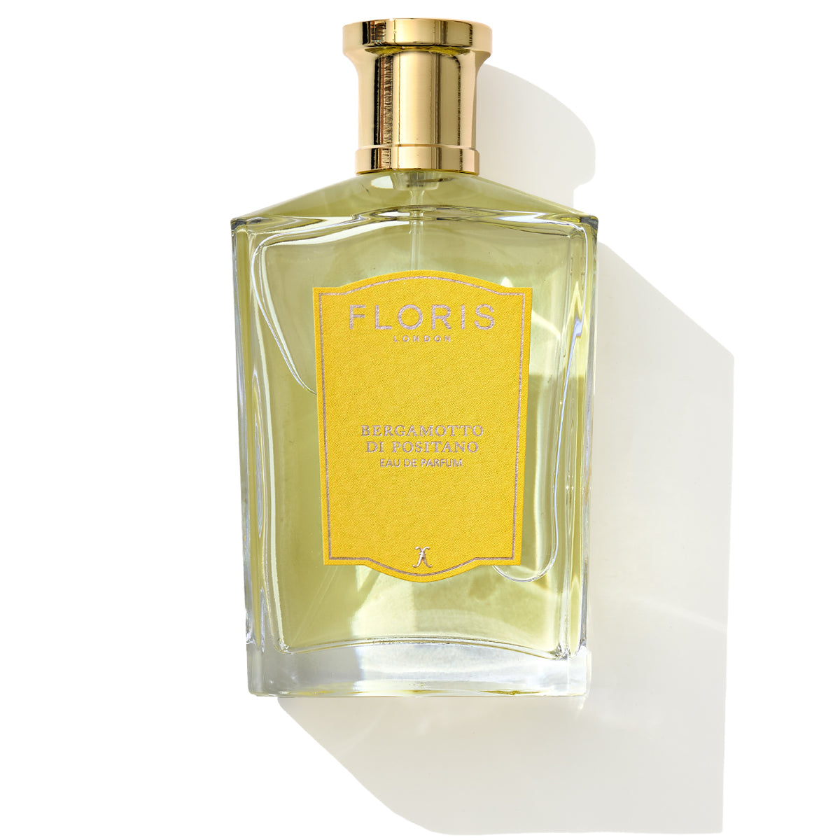 A clear glass bottle with a golden cap, labeled "Bergamotto di Positano - Eau de Parfum" by Floris London. The yellow perfume inside evokes the Mediterranean scent of fresh bergamot and orange blossom. The bottle casts a shadow on the surface.