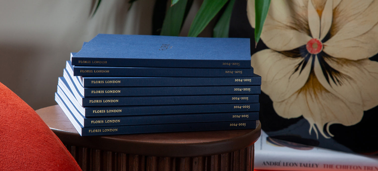 A stack of Floris London's 2024/25 catalogues sits upon a wooden plinth in front of a burnt orange chair.