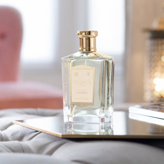 A clear glass bottle of Floris London Bouquet de La Reine eau de toilette with a gold cap sits gracefully on a tray in a softly lit room.