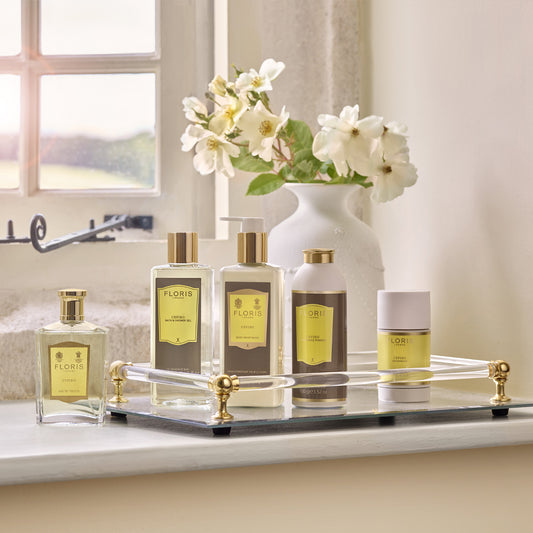 Five Floris London toiletries, including Cefiro Eau de Toilette, rest on a tray beside white flowers in a softly lit room.