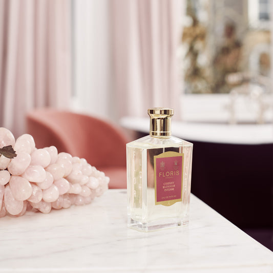 A bottle of Floris London Cherry Blossom Intense Eau de Parfum sits on marble with pink stones, evoking a spring-ready cherry blossom scent.