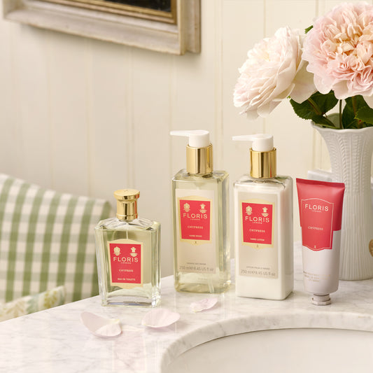 Floris London’s Chypress - Eau de Toilette sits atop a marble sink, surrounded by pale flowers and petals in a softly lit bathroom.