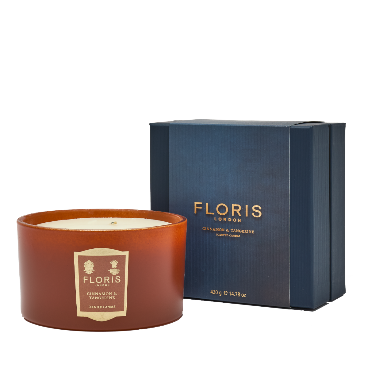 The Floris London EU Cinnamon & Tangerine Deluxe Three Wick Candle rests by its blue box, bringing cozy fragrance to a crisp white setting.