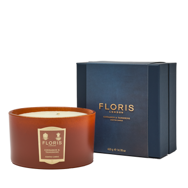 The Floris London EU Cinnamon & Tangerine Deluxe Three Wick Candle rests by its blue box, bringing cozy fragrance to a crisp white setting.