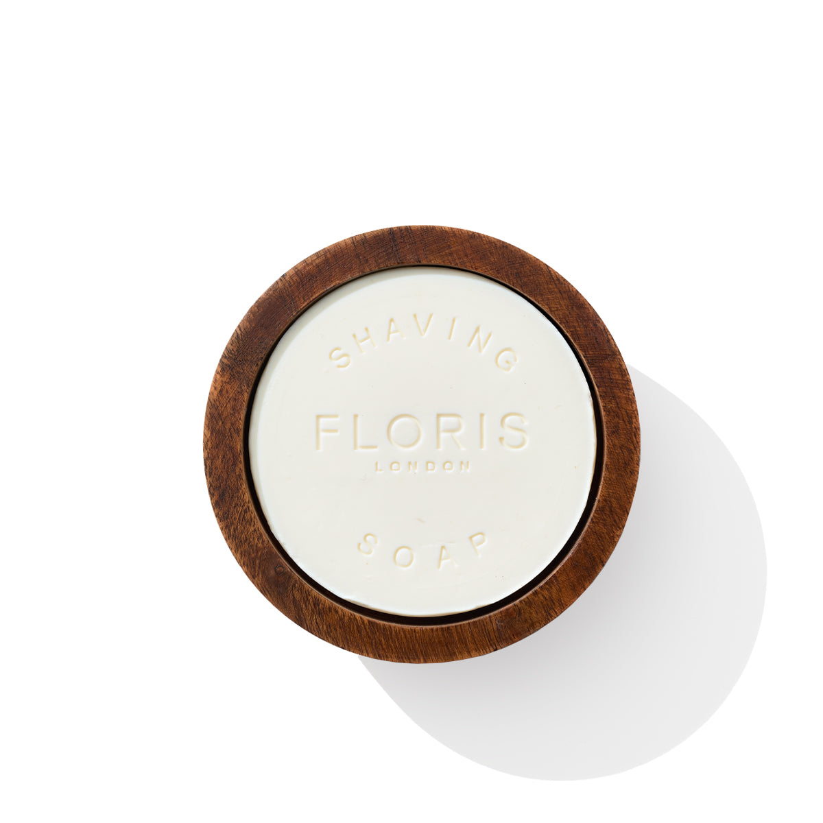 An Elite shaving soap by Floris London is nestled gracefully in a wooden bowl, captured from above against a spotless white surface.