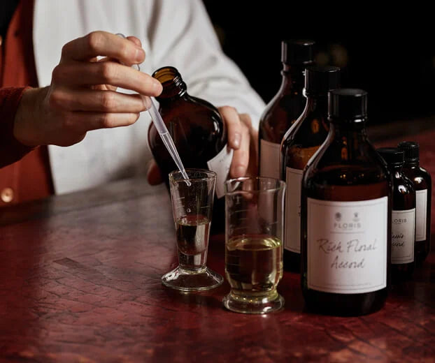 A person uses a dropper to pour liquid into a measuring glass for a Fragrance - Customisation Replenishment 3 x 10ml Trilogy, surrounded by amber glass bottles.