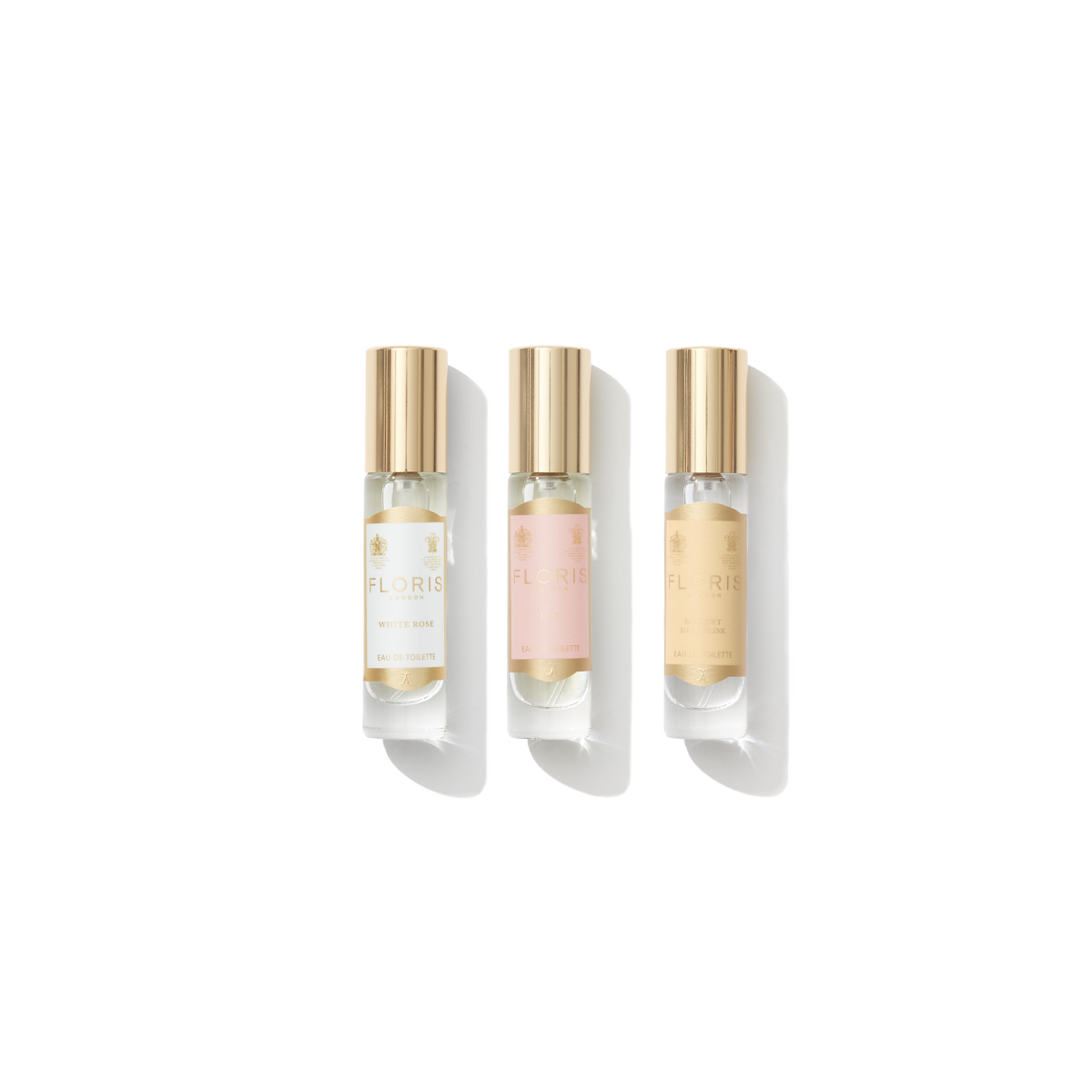 Three small perfume bottles with gold caps, proudly labeled "Floris London EU." From left to right: a pink label, a white label, and a beige label, each elegantly showcasing the brand. This stunning collection, named "Perfumer's Trilogy: For Her," celebrates the finest fragrances in an exquisite array.