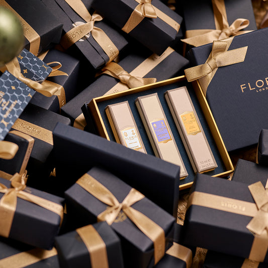 Neatly stacked black gift boxes with gold ribbons, featuring Floris London EU's "Perfumer's Trilogy: For Her," three floral fragrances in a gold-trimmed holder.