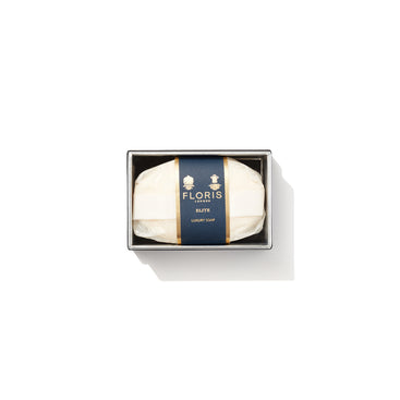 A bar of Floris London EU Elite Soap with a woody scent, wrapped in white paper with a dark blue and gold label, sits boxed on a white background.