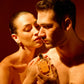 A woman stands close behind a man, touching his shoulder as he holds Floris London’s Golden Amber Eau de Parfum—its floral scent lingers in the air.