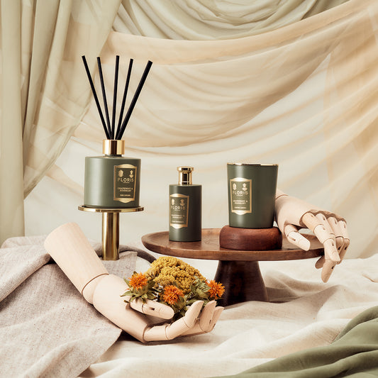 Floris London’s Grapefruit & Rosemary room fragrance set features a reed diffuser, bottle, and candle in green, displayed with dried flowers and mannequin hands.