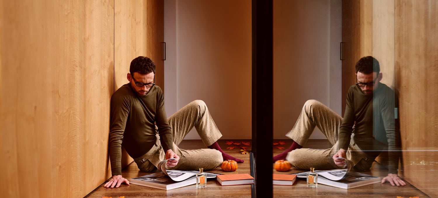 A man sat on the floor reading a book next to a bottle of 'Special No. 127' and autumn foliage.