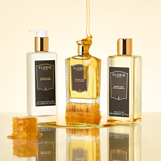 Three Floris London Honey Oud bath products are set with English honeycomb and golden honey dripped over the Honey Oud - Eau de Parfum bottle on yellow.