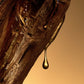 A close-up of golden Celest - Eau de Parfum by Floris London EU, glistening on wood against a warm, brown background.