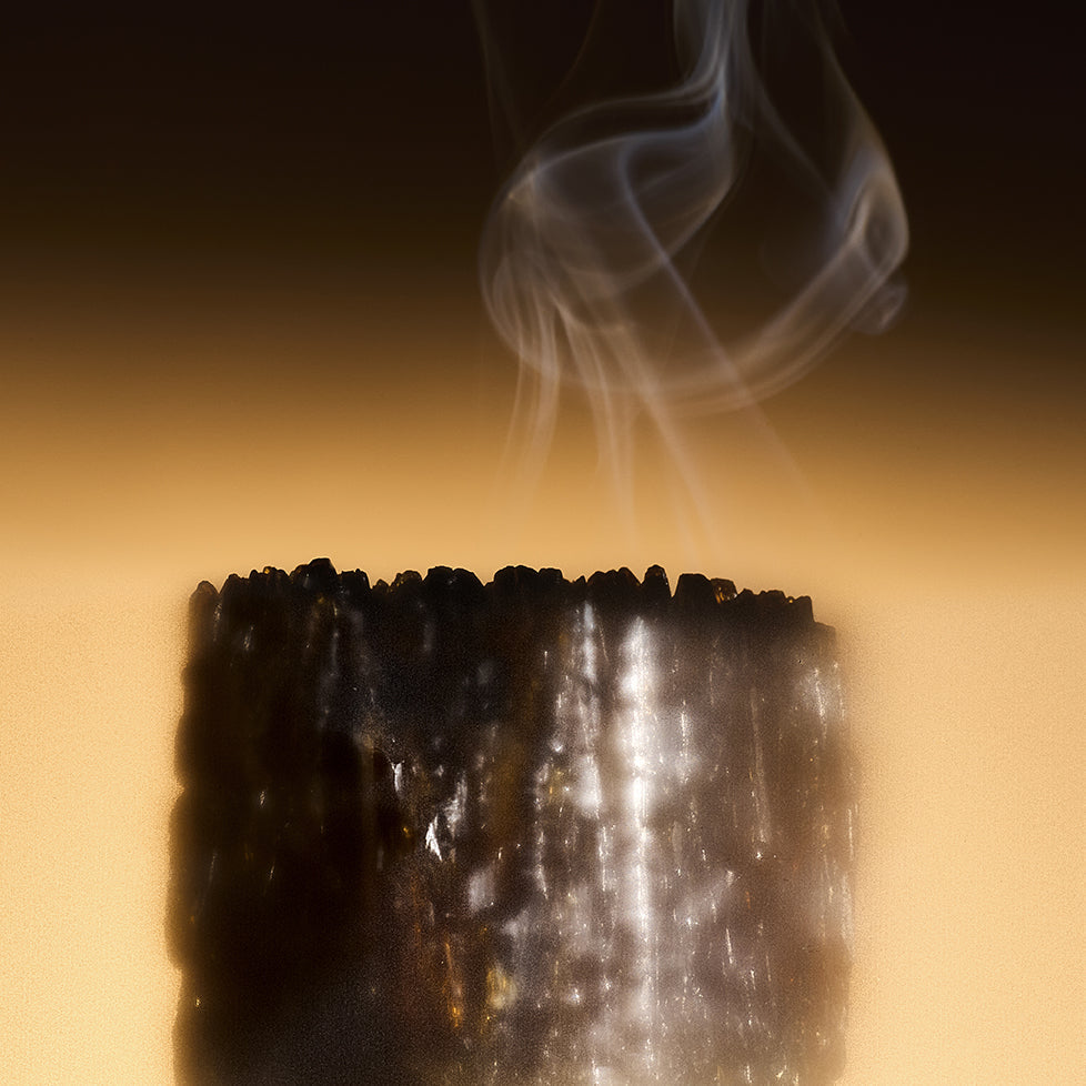 Celest - Eau de Parfum by Floris London EU sits by a burned candle, thin smoke rising against a golden-yellow gradient background.