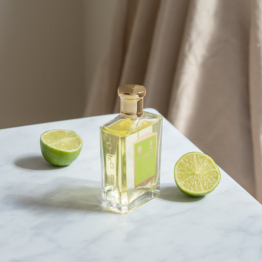 A glass bottle of Floris London Limes - Eau de Toilette with a gold cap sits on marble beside lime halves, suggesting a fresh citrus scent.