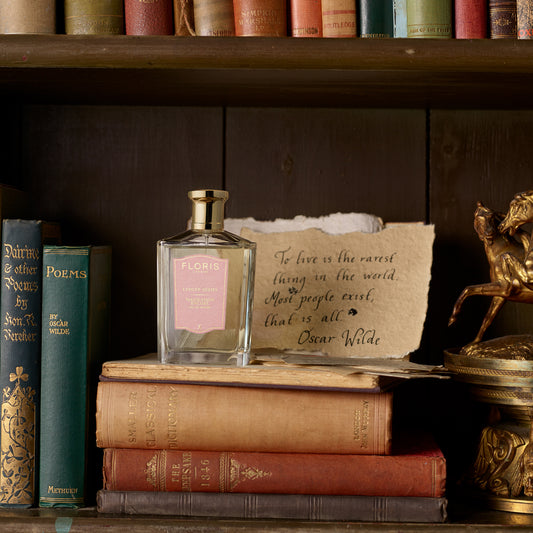A bottle of Malmaison Encore by Floris London EU rests on vintage books next to a handwritten Oscar Wilde quote and a small horse statue.