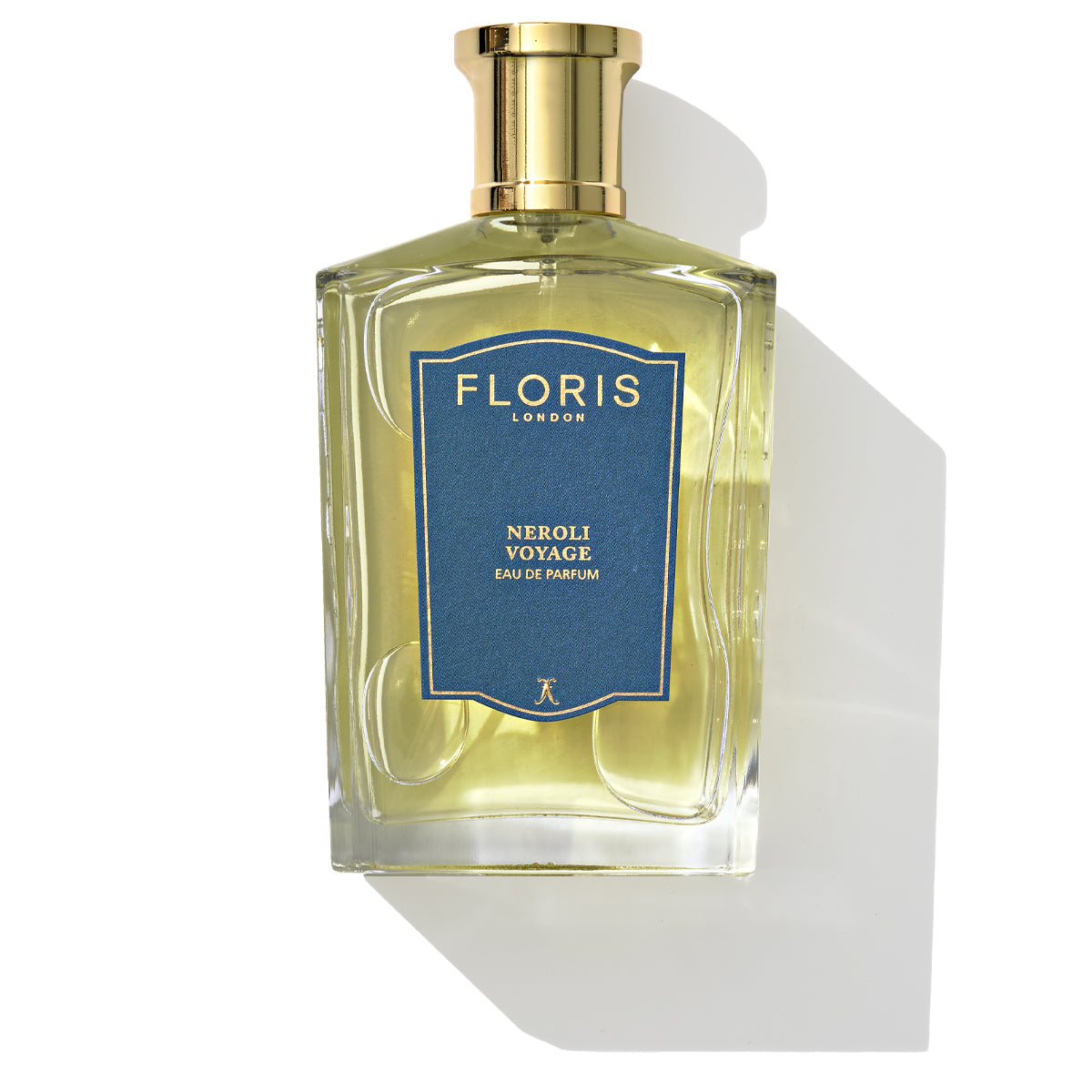 A clear rectangular glass bottle of Floris London Neroli Voyage - Eau de Parfum, a unisex citrus marine fragrance, features a gold cap and a blue label, casting a shadow on a white surface.