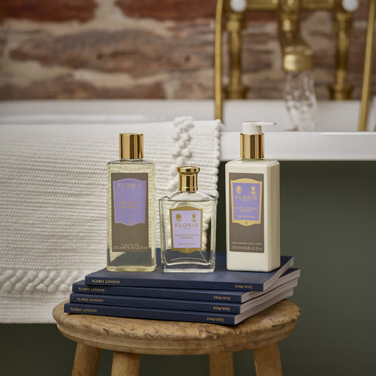 Floris London's Night Scented Jasmine Eau de Toilette, with gold accents and Mediterranean blooms scent, sits on navy notebooks by a bathtub.