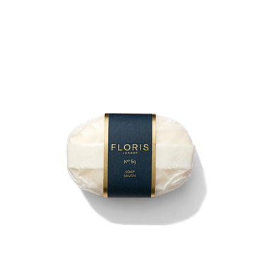 A wrapped bar of Floris London EU No. 89 Soap, with a dark label featuring the brand name and product information in gold and white text, is placed against a white background.