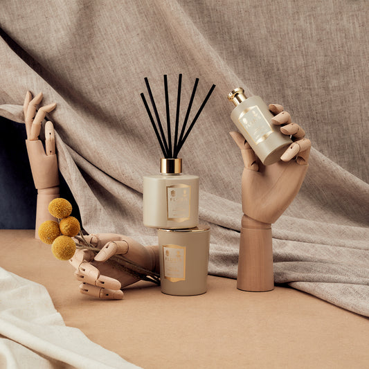 Floris London Oud & Cashmere Reed Diffuser, candle, and spray styled with wooden mannequin hands on beige fabric for a refined home fragrance display.
