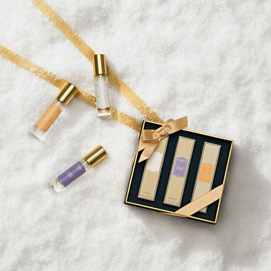 The Perfumer's Trilogy: For Her gift box by Floris London EU features three perfumes and three rollerballs, arranged on snow with gold ribbon for the holidays.