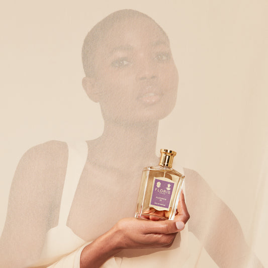 A woman in a cream top holds Floris London EU’s Platinum 22 - Eau de Parfum, partially obscured by sheer beige fabric.