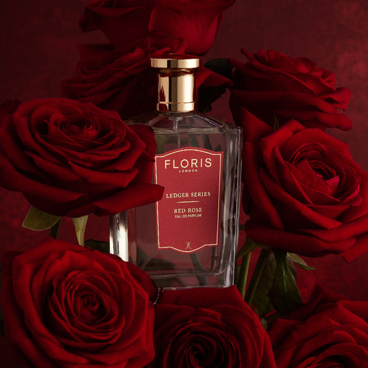 A bottle of Floris London EU Red Rose Eau de Parfum sits among deep red roses, set against a matching red background.