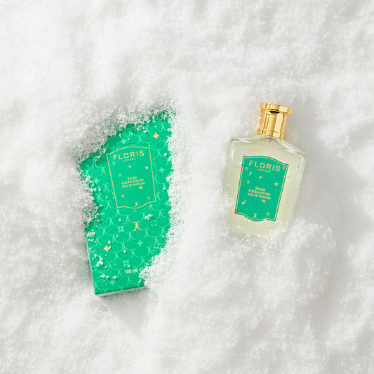 A Floris London EU Rose Geranium | Limited Edition perfume bottle and its green, gold-accented box rest partially buried in snow on a white background.