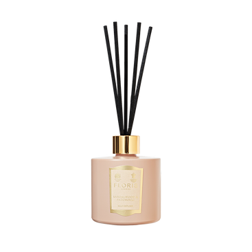 A beige Floris London reed diffuser with black reeds and gold details, labeled "Sandalwood & Patchouli" for a woody amber scent experience.